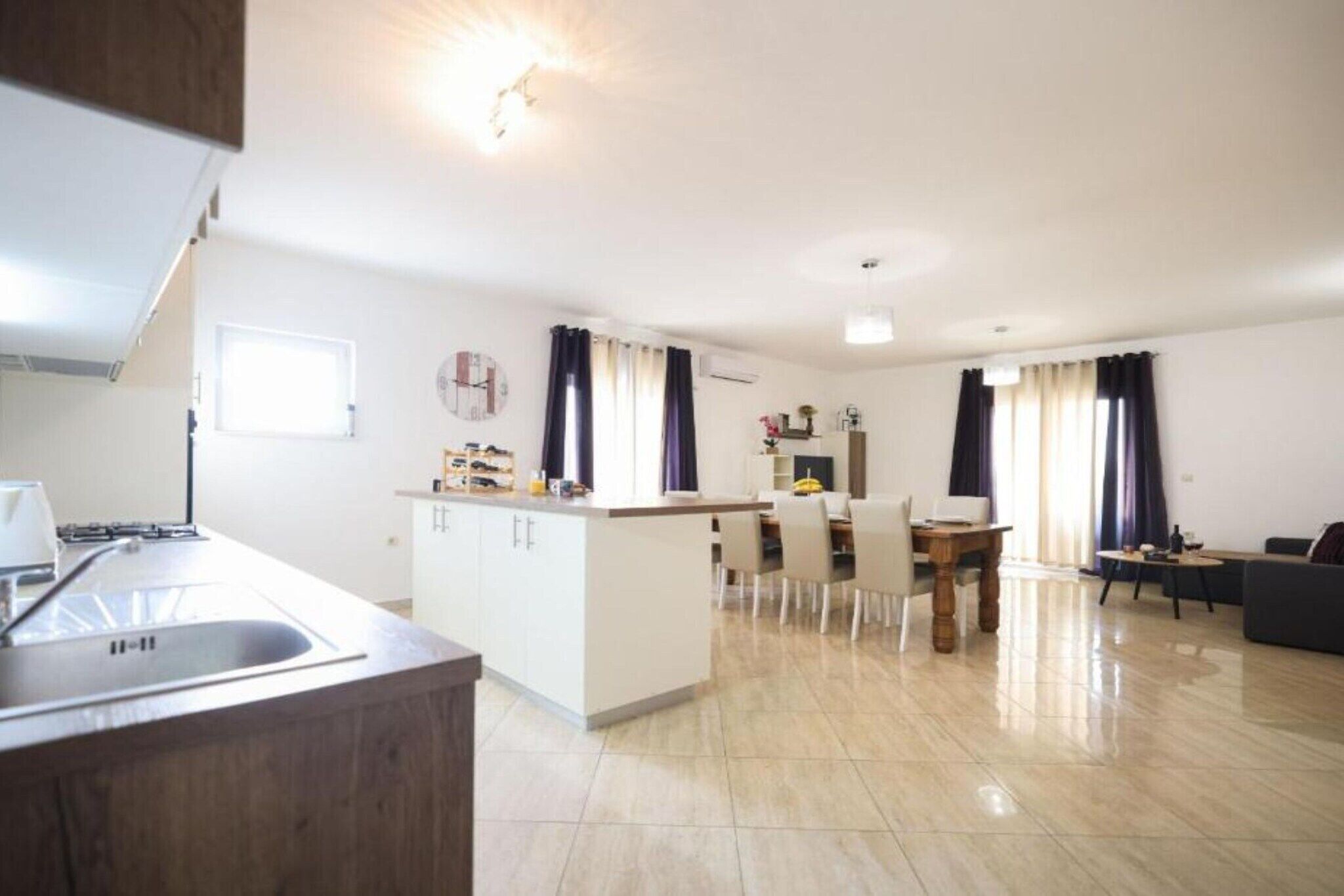 Eine moderne Küche mit Kochinsel, ein Essbereich mit Tisch und Stühlen sowie ein Wohnbereich mit Sofa und Fernseher.