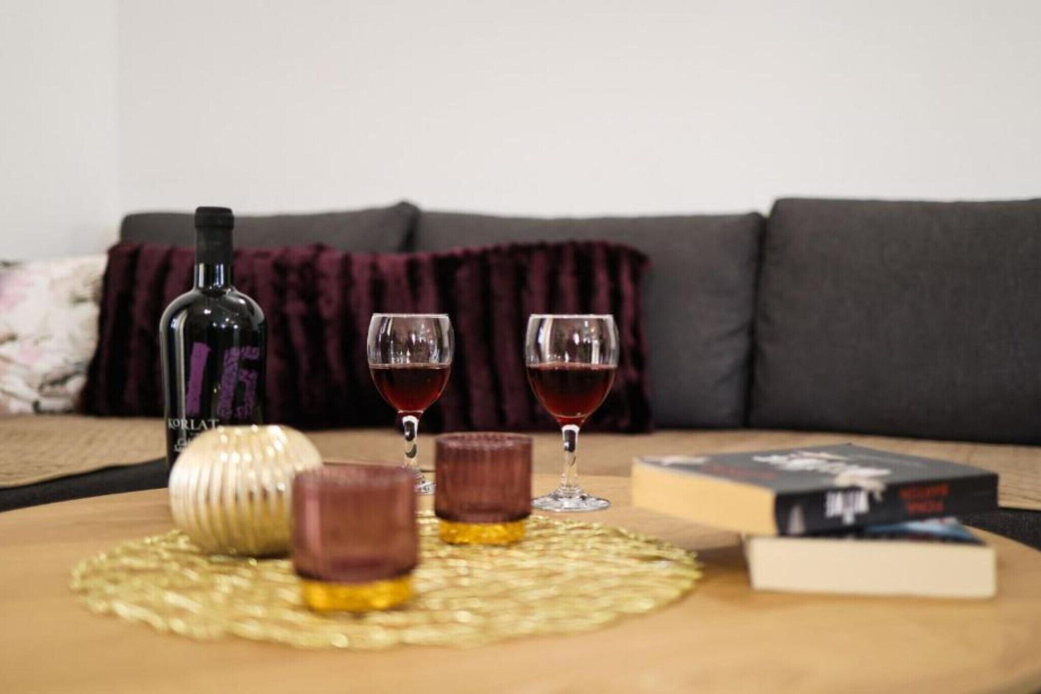 A table with a bottle, two glasses of red wine, and a book on a woven placemat.