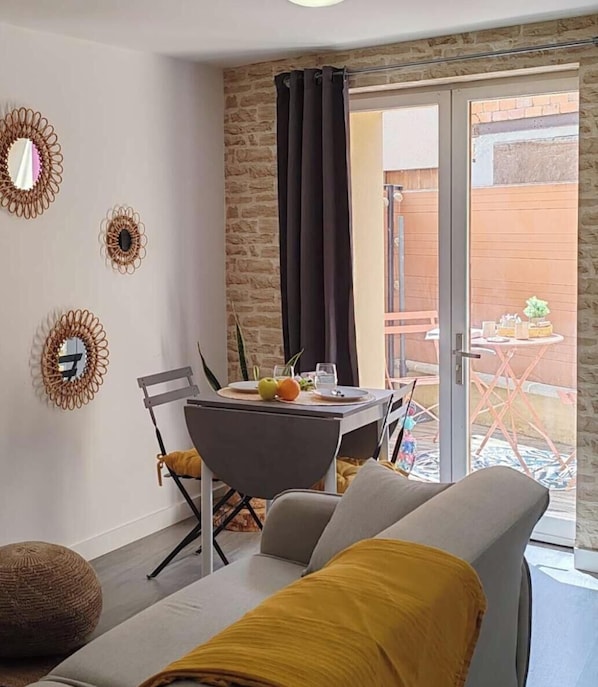 Una habitación moderna con cama, una mesa de comedor con sillas, un pequeño balcón con mesa y sillas, y espejos decorativos en la pared.