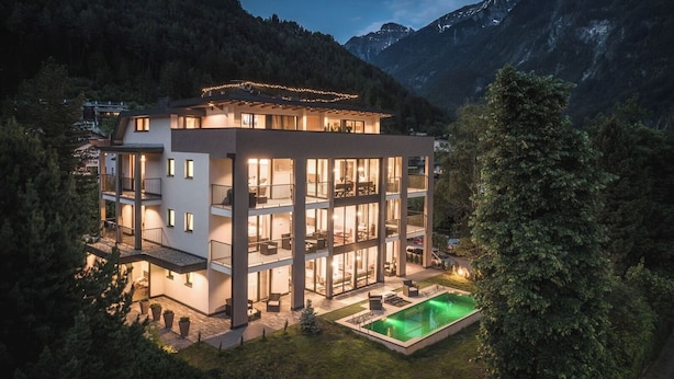 Ein modernes Mehrfamilienhaus mit Balkonen, einem Swimmingpool und einer Bergkulisse.