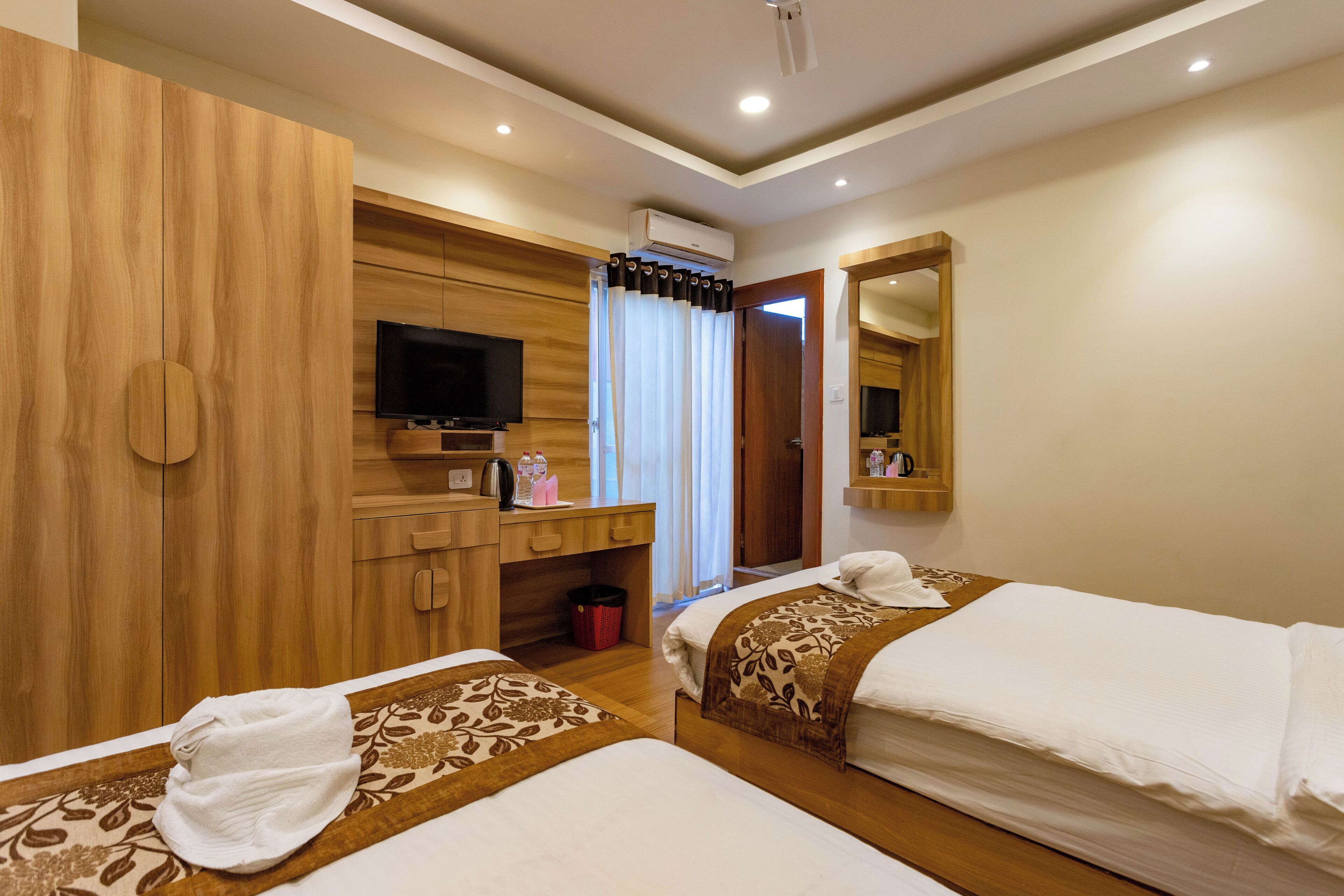 A hotel room with two beds, a TV, a desk with a computer, a mirror, and a window with curtains.