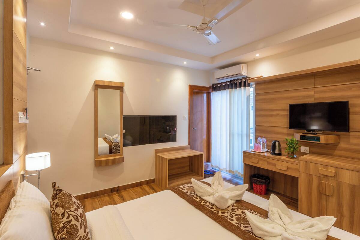Une chambre d’hôtel moderne avec un grand lit, une télévision, un bureau en bois et un ventilateur de plafond.