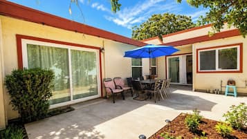 A residential patio with a table and chairs, a blue umbrella, and a small garden area.