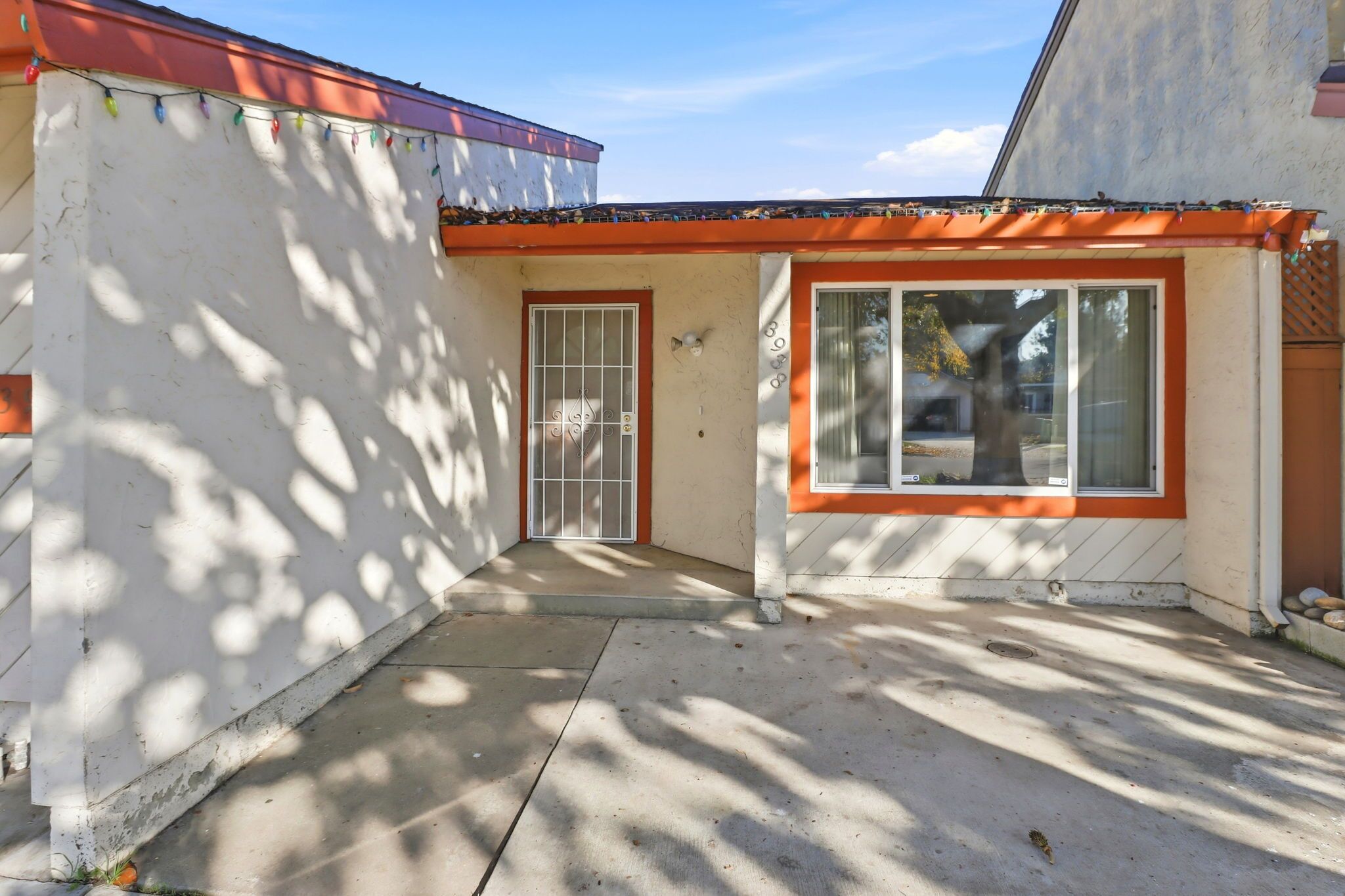 A building with a white exterior and orange trim, featuring a door with a metal gate and a window with a view of the outside.