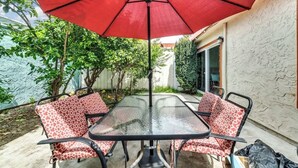 Une terrasse avec une table et des chaises en verre, un parasol rouge et un mur blanc.