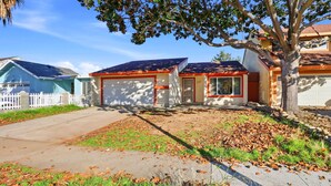 A residential property with a front yard, a white picket fence, and a driveway leading to a garage.