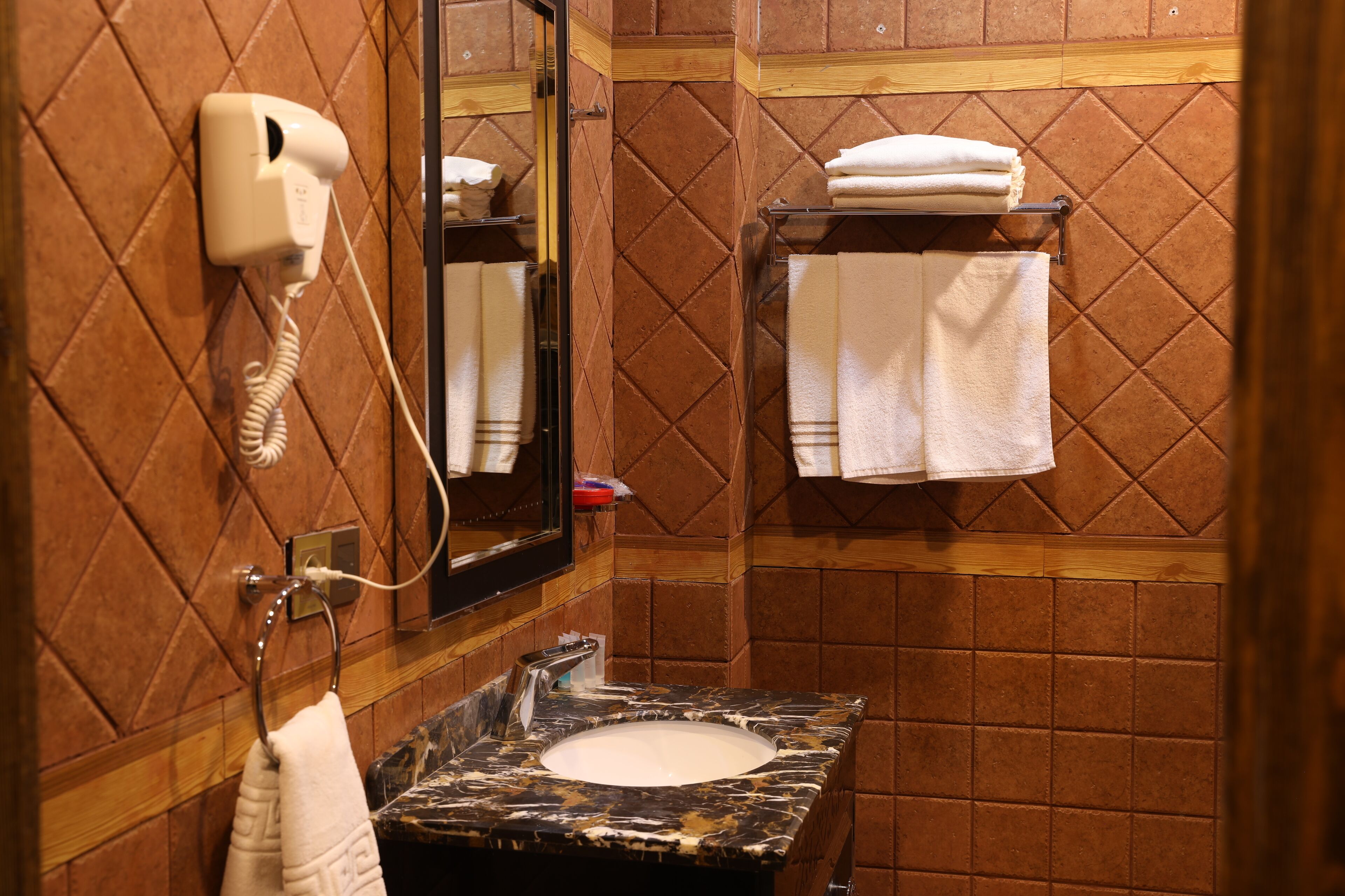 A bathroom with a marble sink, a hairdryer, and a towel rack with folded towels.