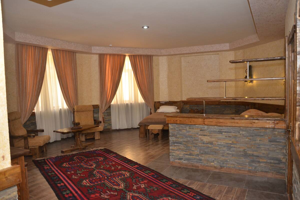 A spacious room with a large bed, a wooden bench, and a stone fireplace.