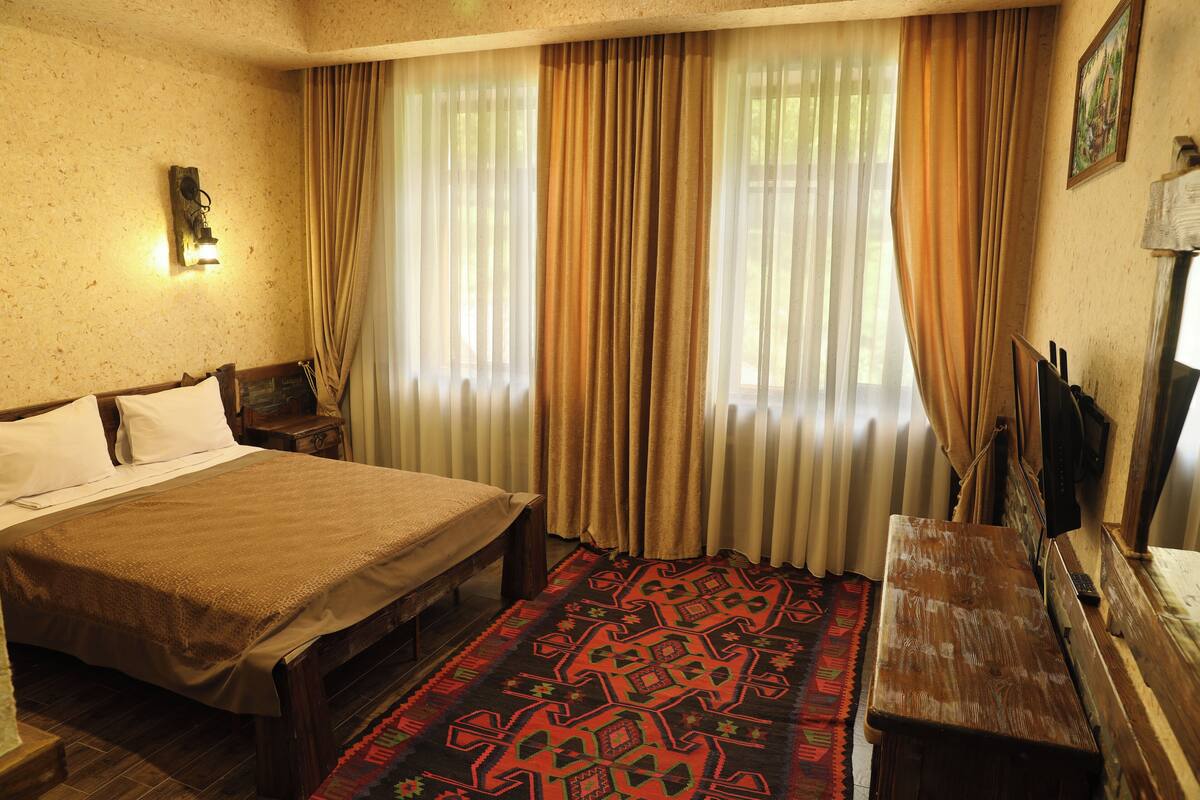 A room with a large bed, a wooden bench, a patterned rug, and a wall-mounted TV.