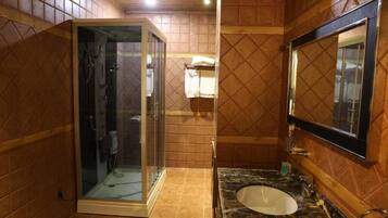Une salle de bain dotée d’une douche à parois de verre, d’un lavabo avec un plan de travail en marbre et d’un miroir au-dessus du lavabo.