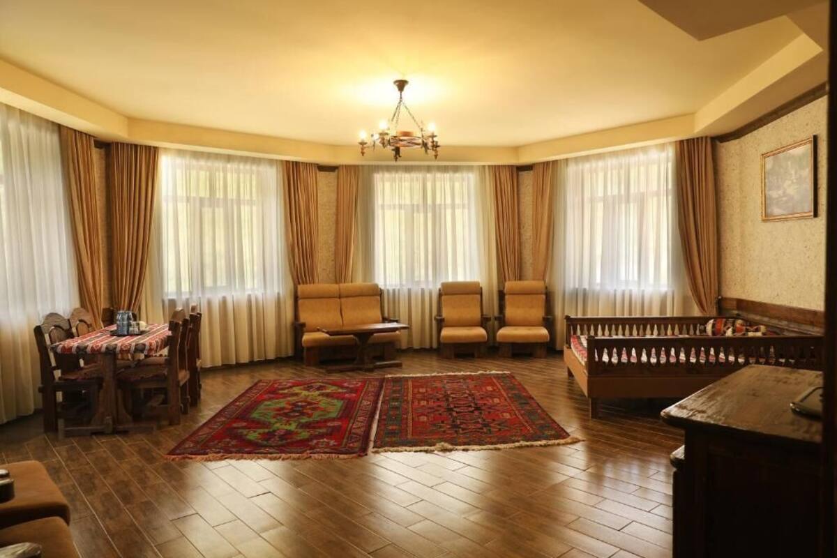 A living room with a wooden floor, a dining table with chairs, a sofa, a bench, and a chandelier.