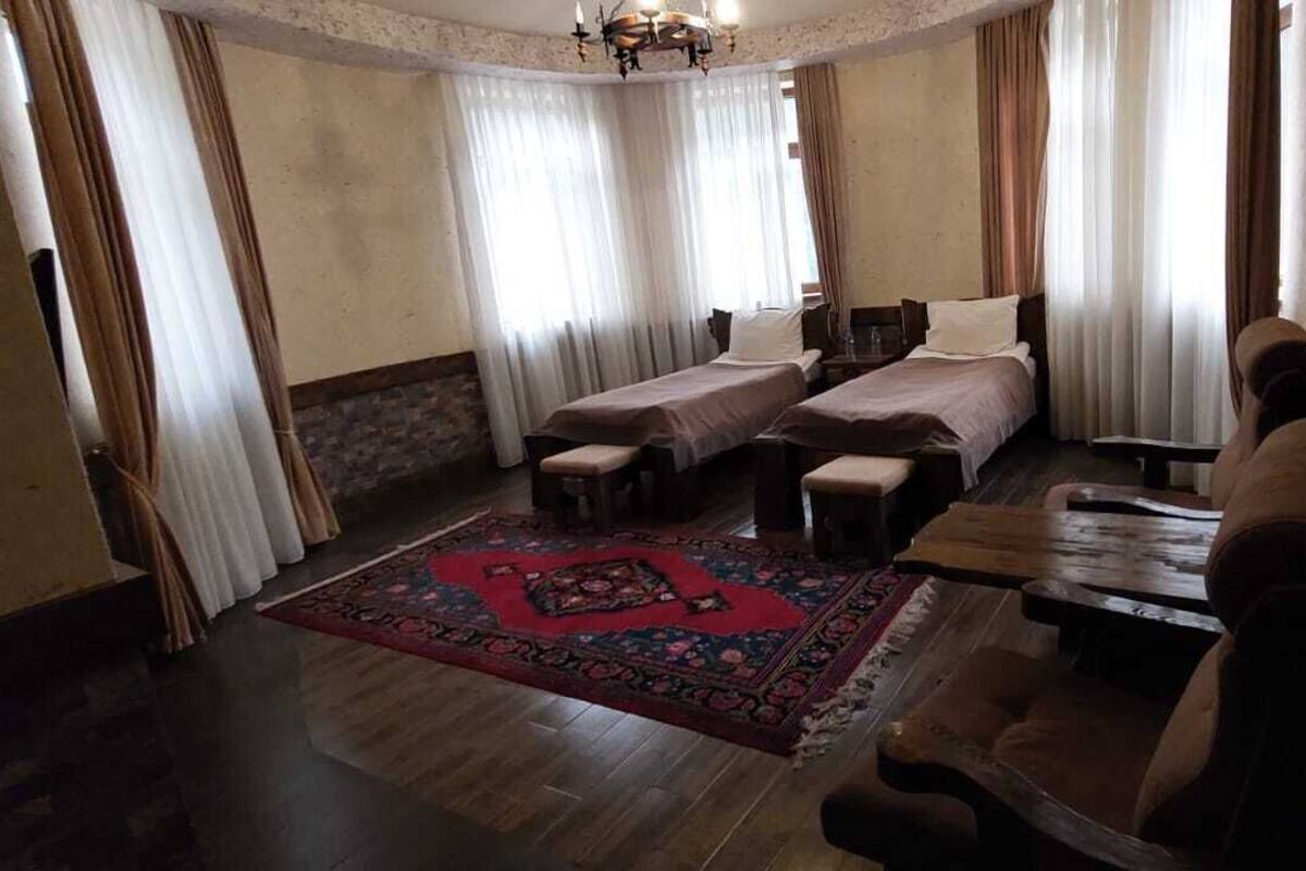 A hotel room with two single beds, a wooden bench, a small table, and a patterned rug.