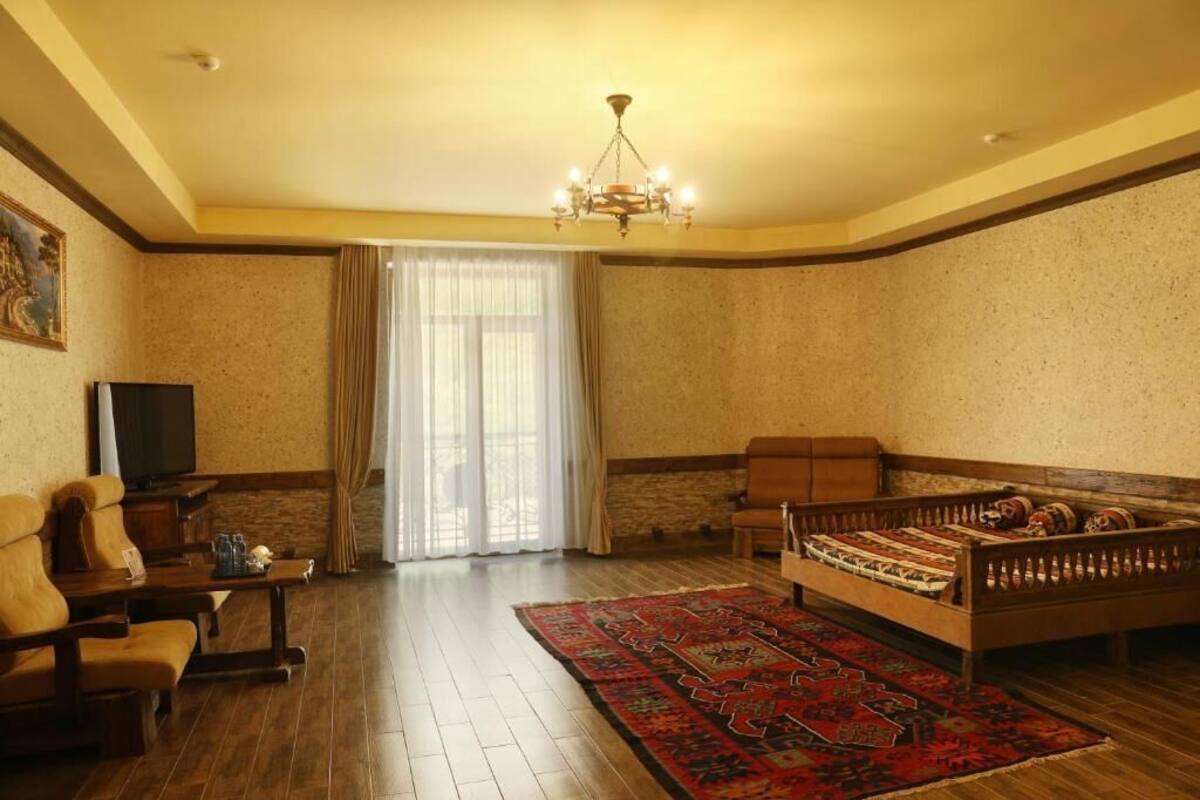 A spacious living room with a wooden floor, a sofa, a television, and a large window with curtains.