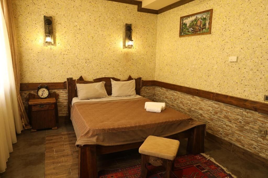 A bedroom with a wooden bed, two wall-mounted lights, a clock, and a painting on the wall.