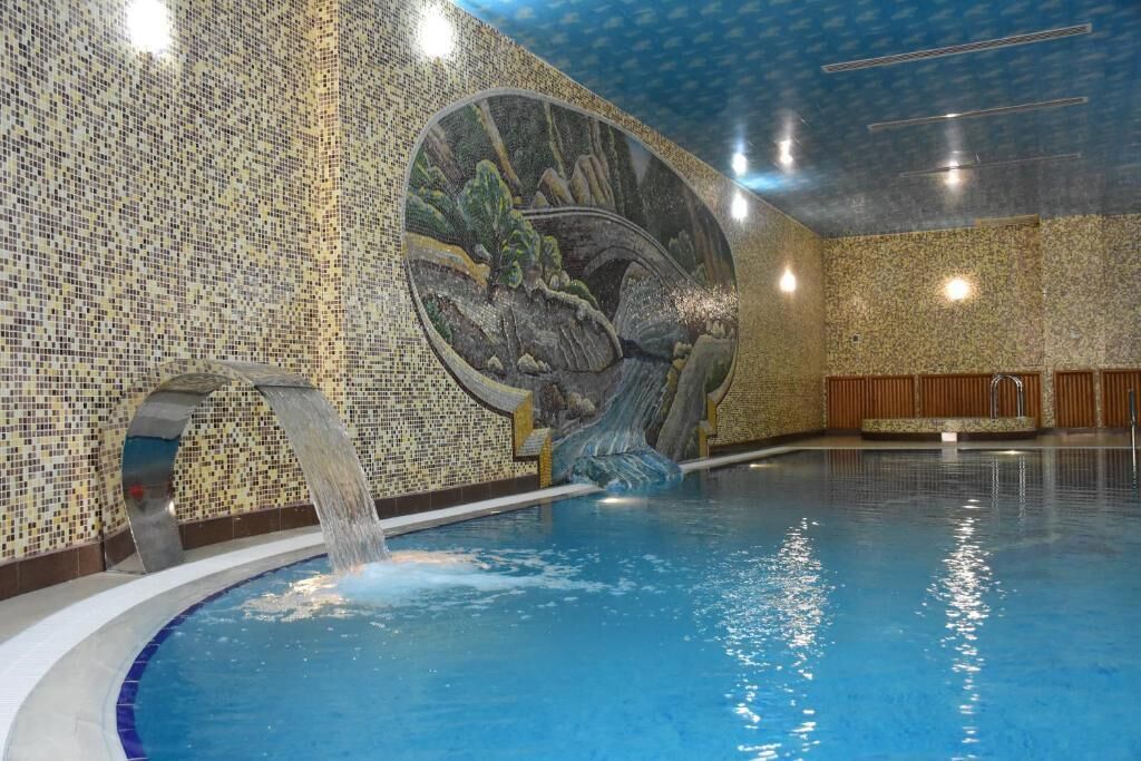 Una piscina interior con pared de mosaicos y una cascada.