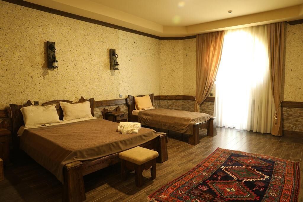 A room with two beds, a bench, a rug, and a window with curtains.