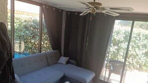 A modern living room with a grey sectional sofa, a small table with a cup and a book, and a ceiling fan. - 🌴 Cocooning Holiday Home - Sunny & Ideally Placed! ☀️🏖️ (Valras-Plage)