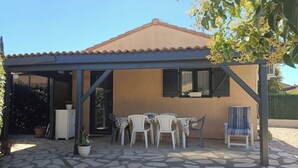 A covered patio with a stone floor, a table with chairs, and a potted plant. - 🌴 Cocooning Holiday Home - Sunny & Ideally Placed! ☀️🏖️ (Valras-Plage)