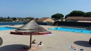 A swimming pool with a thatched-roof structure, surrounded by a sandy area with a few people and towels. - 🌴 Cocooning Holiday Home - Sunny & Ideally Placed! ☀️🏖️ (Valras-Plage)
