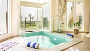 A modern indoor swimming pool with glass walls, a blue and white towel, and a pair of slippers on the floor.