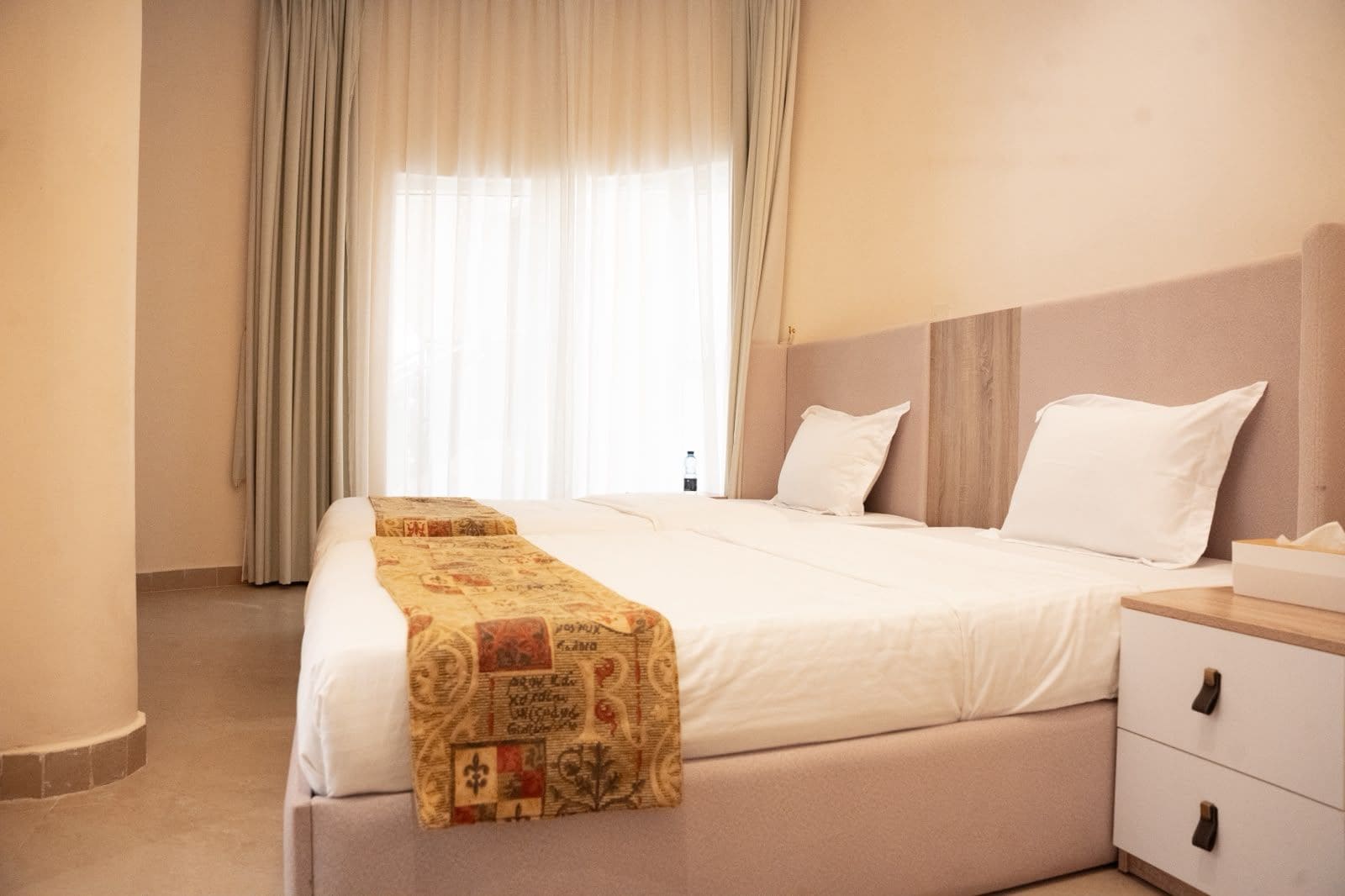 A hotel room with a large bed, a bedside table, and a window with curtains.