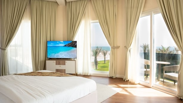 A spacious bedroom with a large bed, a flat-screen TV, and a balcony with a view of the beach.
