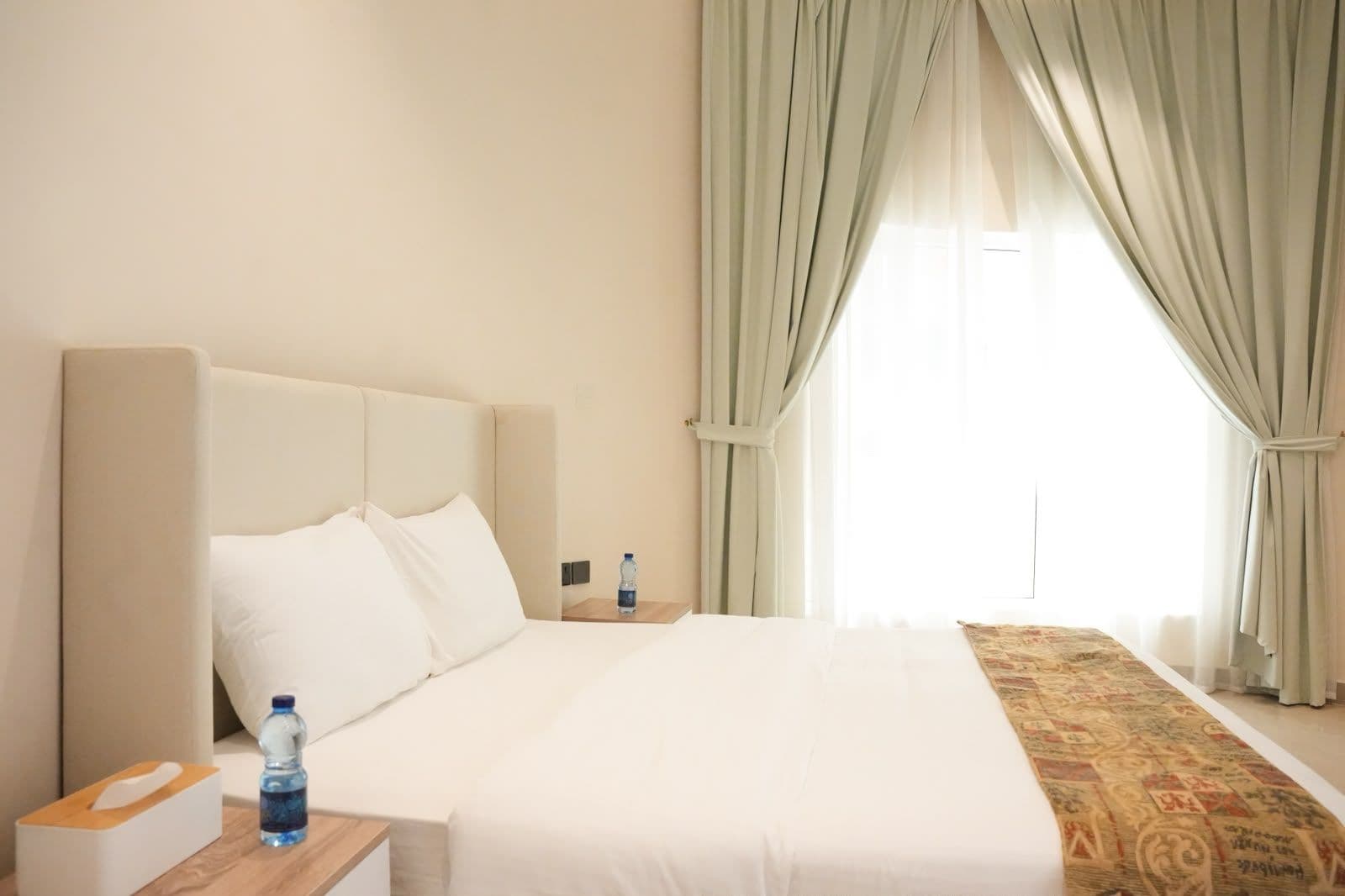 A hotel room with a large bed, a bedside table with a water bottle, and a patterned rug.