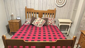 Un dormitorio con una cama de madera, una mesita de noche con un reloj, una mesilla auxiliar y un papel tapiz estampado.