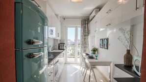 A modern kitchen with a teal refrigerator, white cabinets, and a dining area with a table and chairs. - Alimos Marina Home Luxury Corner SeaView Apartment (Alimos)