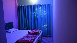 Una cama individual en una habitación con cabecera, una mesita de noche y una ventana con cortinas azules.