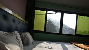 Una cama con cabecera, una ventana que da a edificios y colinas, y una cortina.
