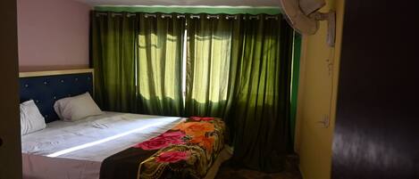A bedroom with a bed, green curtains, a ceiling fan, and a patterned bedspread.