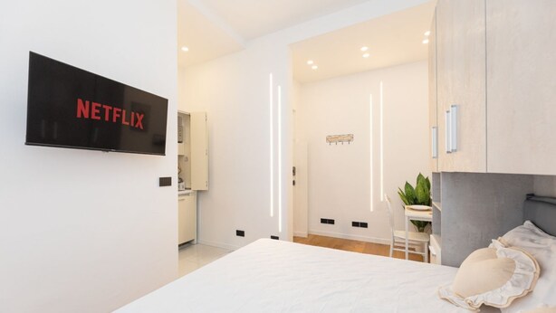 Ein modernes Hotelzimmer mit einem großen Bett, einem an der Wand montierten Fernseher, einem Schreibtisch und einem Sessel.