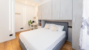 Ein modernes Schlafzimmer mit einem großen Bett, grauen Schränken und einer kleinen Arbeitsnische.