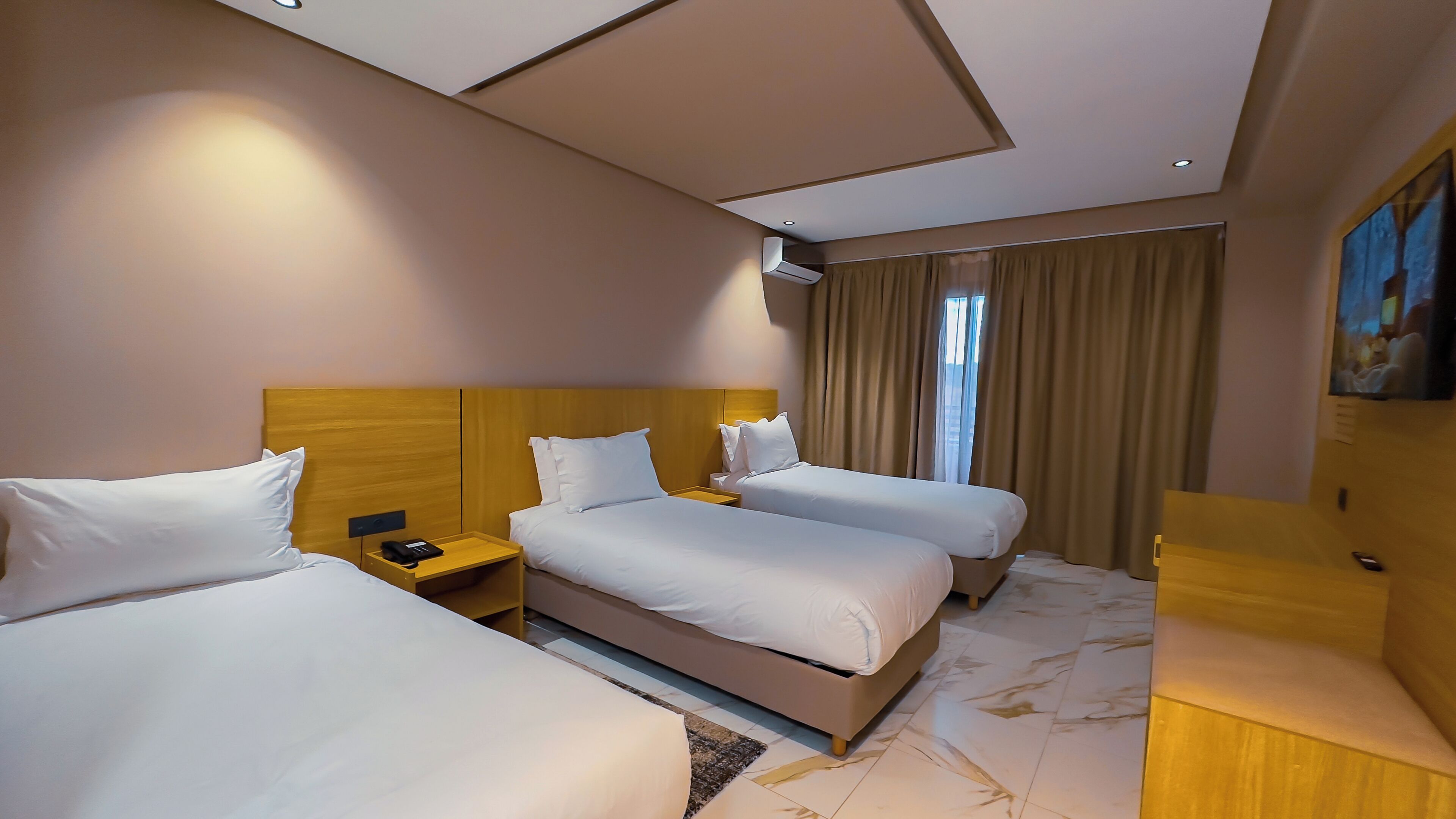 A hotel room with two beds, a wooden headboard, a nightstand with a phone, a painting on the wall, and a window with curtains.