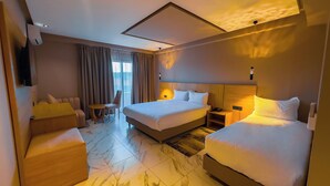 Una camera d'albergo con un letto grande, due letti singoli, un divano, una poltrona, un tavolino e una televisione.