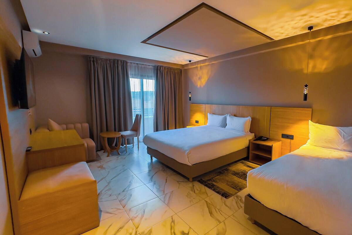 A hotel room with a large bed, two smaller beds, a sofa, a chair, a small table, and a TV.