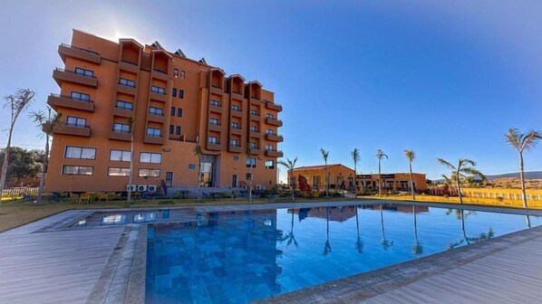 A multi-story hotel with a swimming pool in the foreground. - Hotel Atlas Day (Agoudi N'Lkhair)