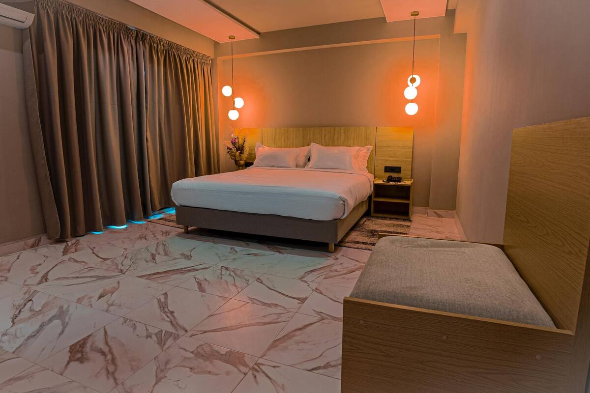 A hotel room with a bed, bedside tables, a chair, and a marble-patterned floor.
