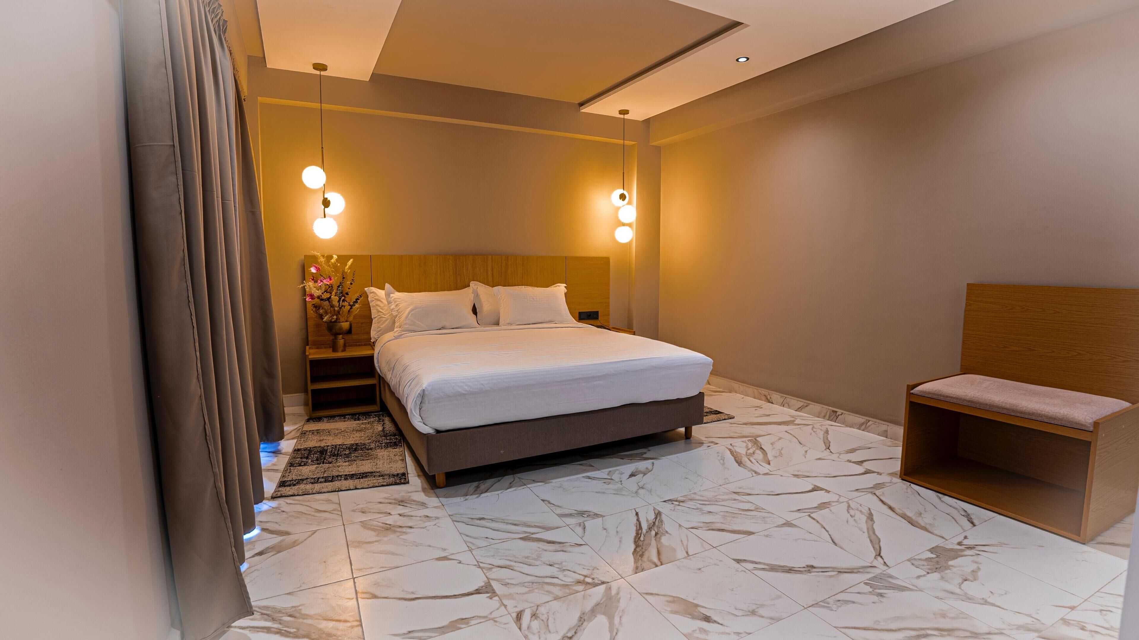 A modern bedroom with a large bed, a bedside table with a vase, and a small wooden bench.