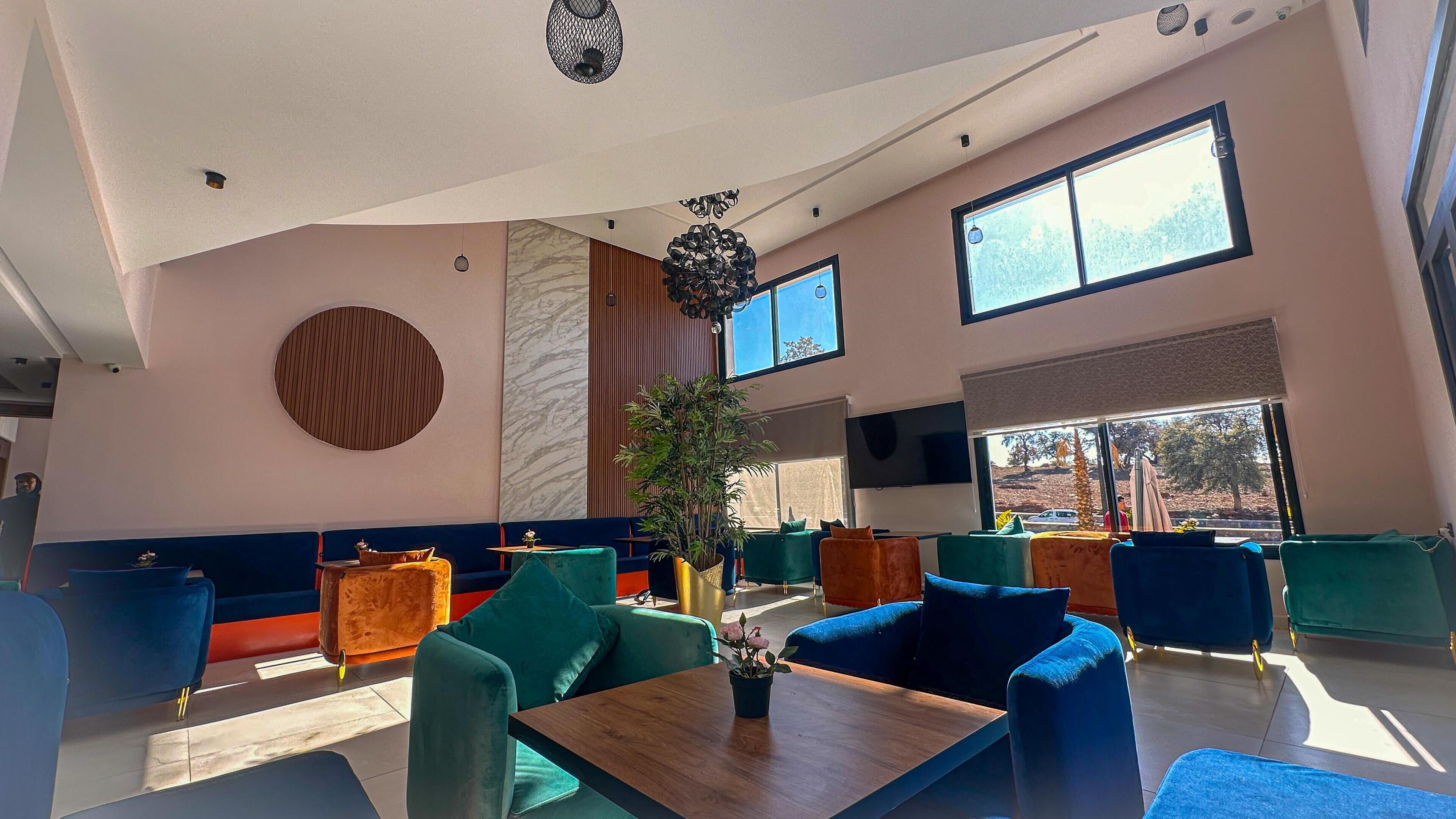A modern lounge area with seating arrangements, a central plant, and large windows providing natural light.