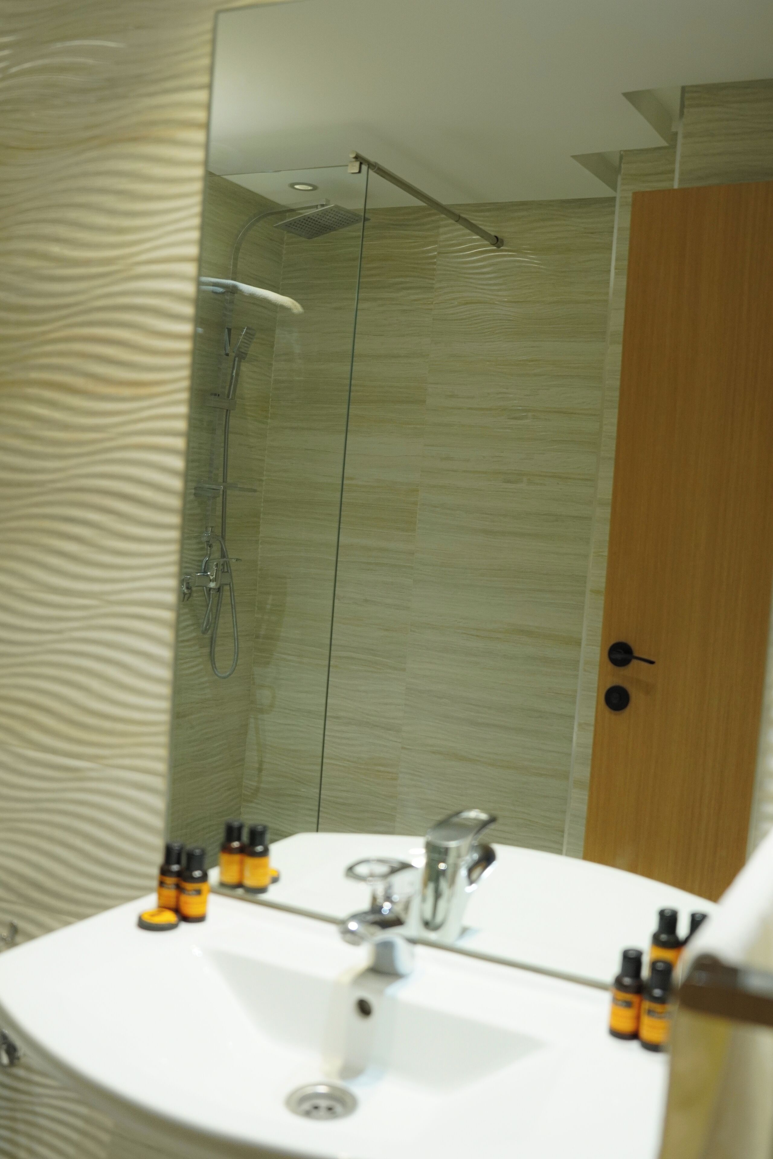 A modern bathroom with a glass-enclosed shower, a round sink with a mirror, and toiletries on the counter.
