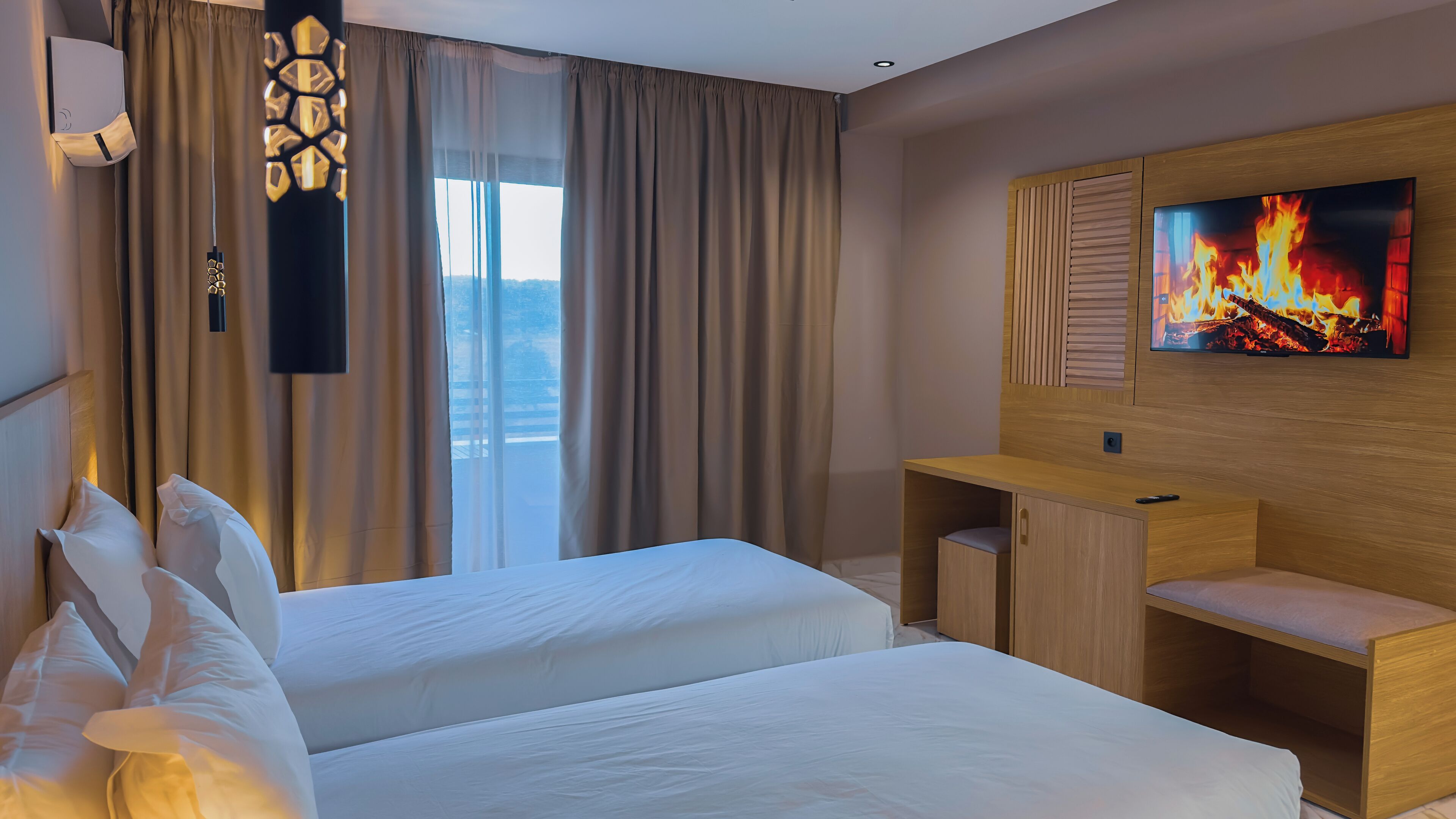 A hotel room with two beds, a TV displaying a fire, and a desk with a chair.