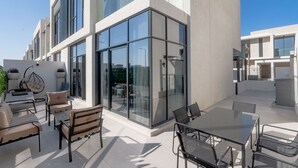 Une terrasse extérieure moderne, dotée de murs en verre, de sièges et d’un fauteuil suspendu.