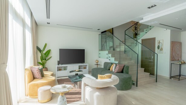 Un salon moderne doté d’un téléviseur à écran plat, de sièges confortables, d’un escalier en verre et d’un design minimaliste.