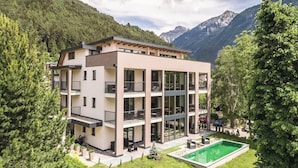 Ein modernes, mehrstöckiges Gebäude mit Balkonen, einem Swimmingpool und einer Bergkulisse.