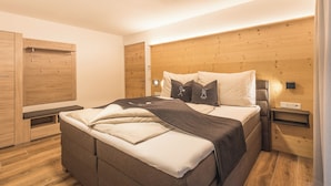 Ein modernes Schlafzimmer mit einem Holzkopfteil, einem Bett mit grau-weißer Bettdecke, einem Nachttisch mit Lampe und einem Holzschrank.