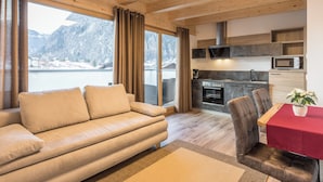 Ein modernes Wohnzimmer mit einer Couch, einem Esstisch mit Stühlen, einer Küchenzeile und einem großen Fenster mit Vorhängen.
