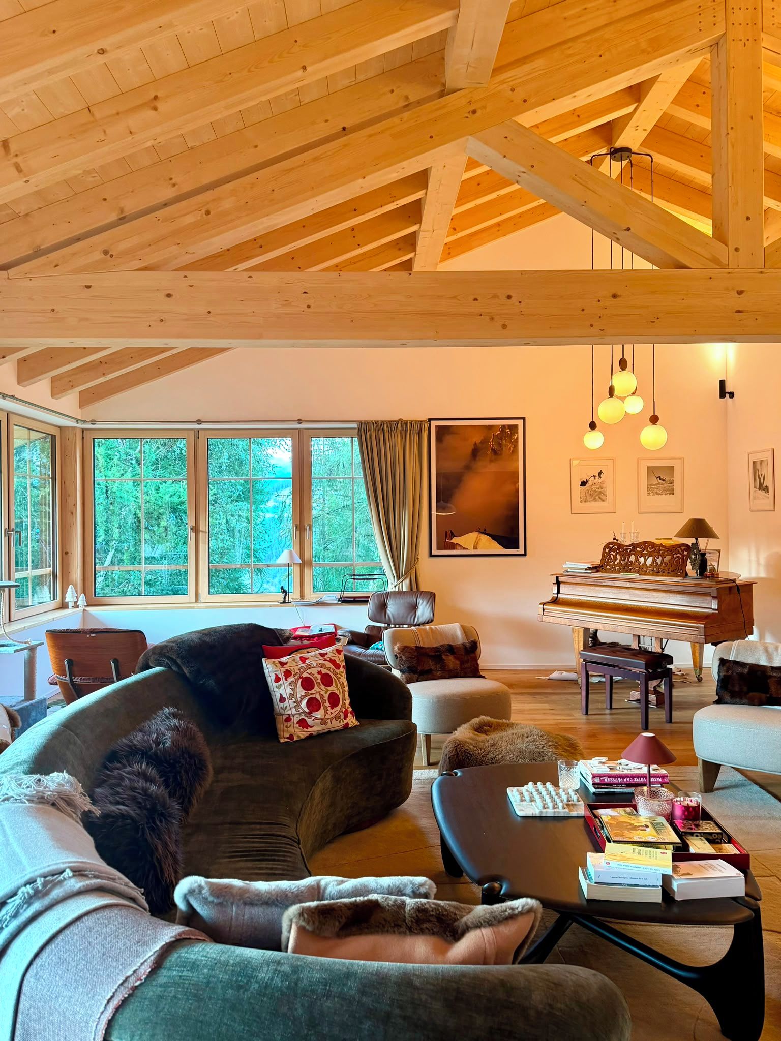 A spacious living room with a high wooden ceiling, a grand piano, and a large window offering a view of greenery.