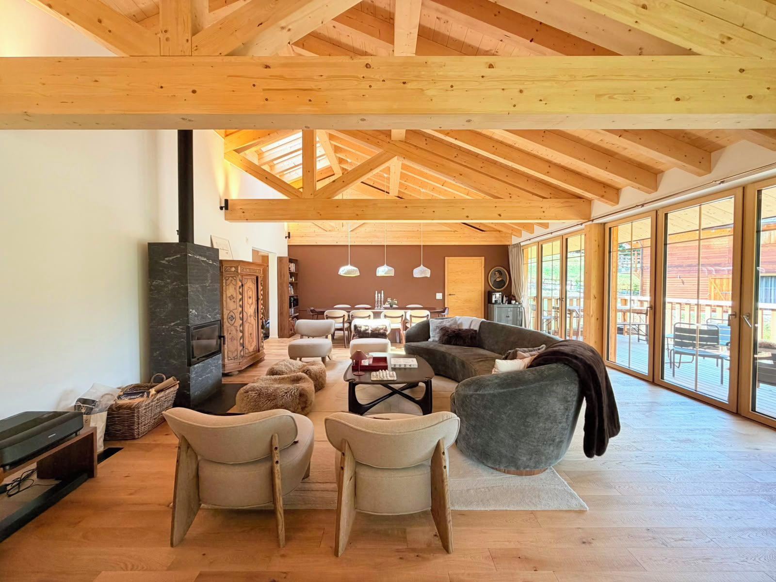 A spacious living area with a high ceiling and large windows, wooden beams, and a fireplace.